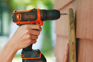 A Black+Decker max drill drilling wood to a house.