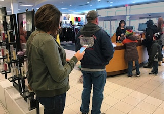 A woman looking down at her cellphone while standing in a line.