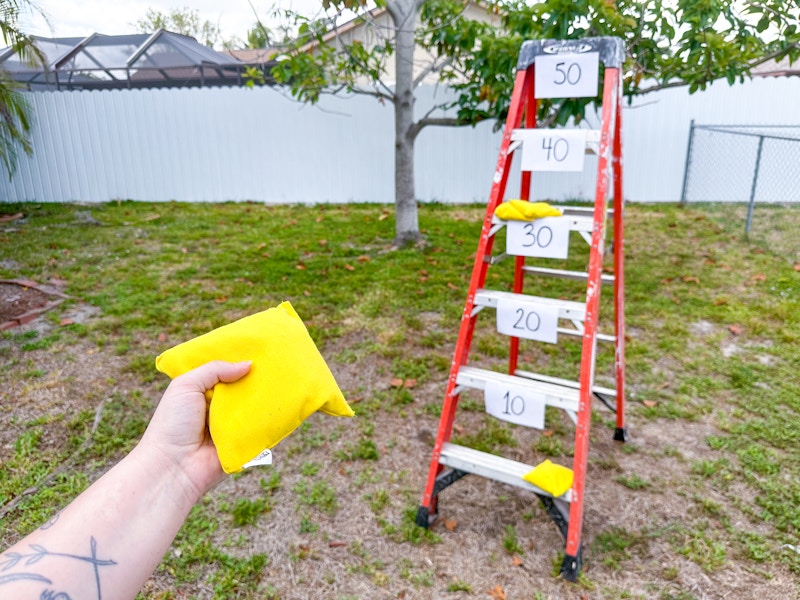 Someone about to toss a bean bag through a ladder with signs taped on each step for up to 50 points