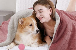 a girl and dog cuddling under a heated blanket