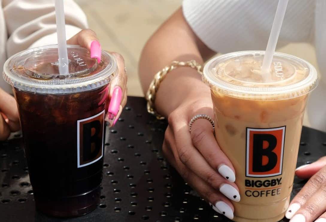 two people sitting and having two iced coffees together for national coffee day at biggby