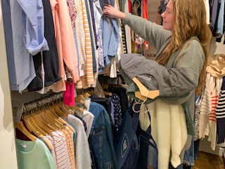A woman shopping searching a clearance rack with clothing in her arms.