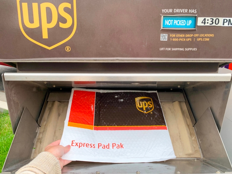 Hand holding UPS Express Pad Pak padded envelope in UPS drop off box