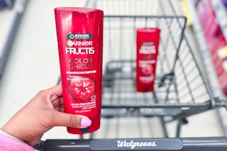 hand holding bottle of Garnier Fructis conditioner in front of shopping cart with another bottle inside