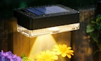 a solar light on a fence outside next to flowers