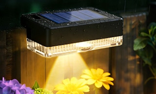 a solar light on a fence outside next to flowers