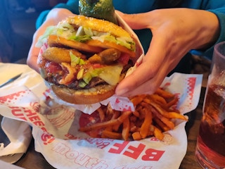A person’s hands holding a very large Jalapeño Burger from Red Robin over a basket with seasoned fries sitting on a table.