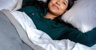 A woman laying under sheet in bed while smiling