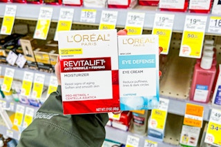 person holding l'oreal moisturizer and eye cream in front of shelves