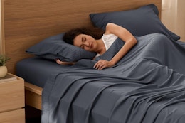 A woman sleeps in a gray cooling sheet set with a fitted sheet, a flat sheet, and two pillowcases