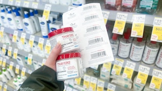 person holding 2 bottles of thayers blemish pads with a stack of paper coupons