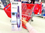 hand holding a shark cyclone hand vacuum in front a target cart