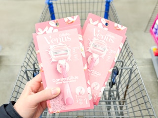 2 Venus ComfortGlide White Tea Razors held over Walmart shopping cart