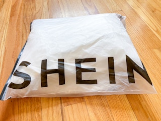 A white shein maxi dress folded in a SheIn shipping bag on the hardwood floor