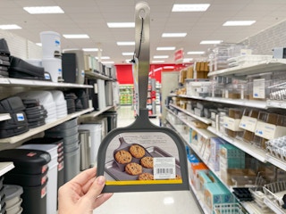 A Wilton Big Cookie spatula held out by hand in front of a store aisle.