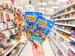 holding 2 packs of friskies lickable cat treats in a target aisle