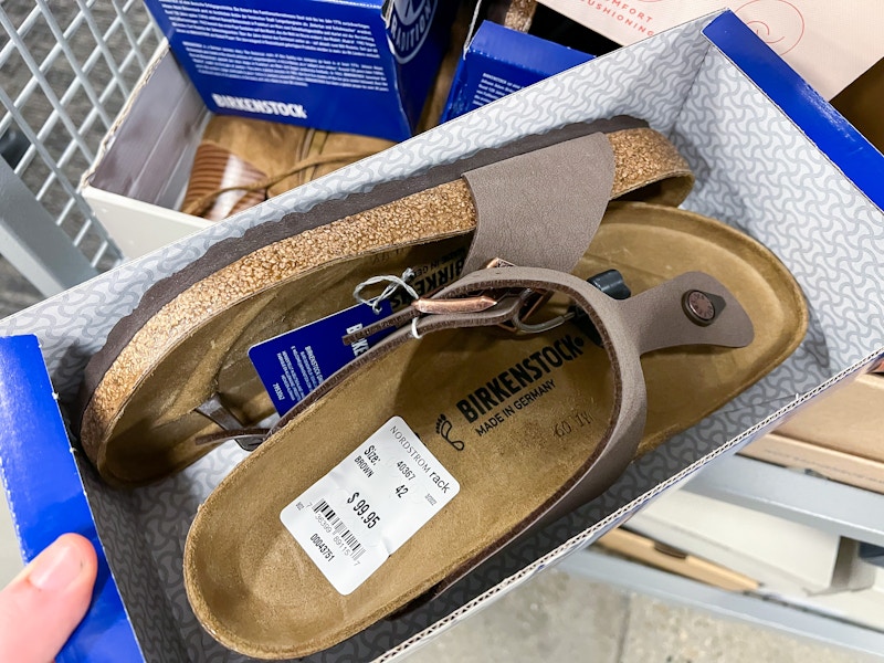 A person's hand holding an open shoebox with a pair of Birkenstock sandals inside.