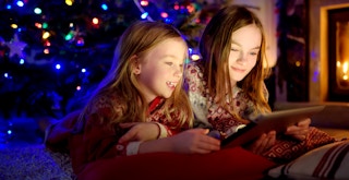 girls lying on living room floor watching christmas movie on tablet feature
