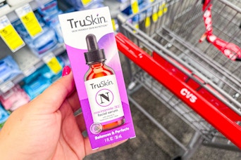 person holding a truskin facial serum over a cvs cart