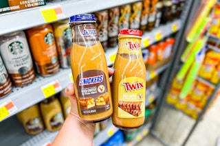 person holding a bottle of snickers and twix flavored iced coffees in front of a shelf