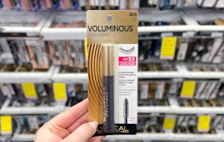 A hand holding a bottle of L'Oreal Voluminous Mascara in a store aisle.