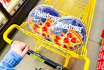 person pushing a shopping cart with tombstone pizza in it