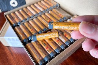 A person holding up an orange amazon basics battery with an open box of batteries in the background.