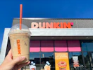 someone holding up a pumpkin spice drink in front of a Dunkin