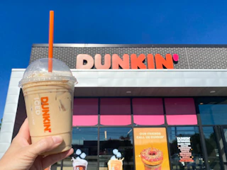 someone holding up a pumpkin spice drink in front of a Dunkin