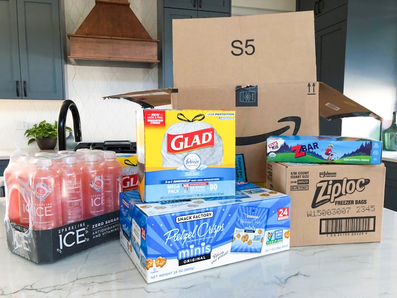 Glad garbage bags, sparking juice, pretzel snack bags, ziploc bags, and zbars sitting on a counter in front of an Amazon box