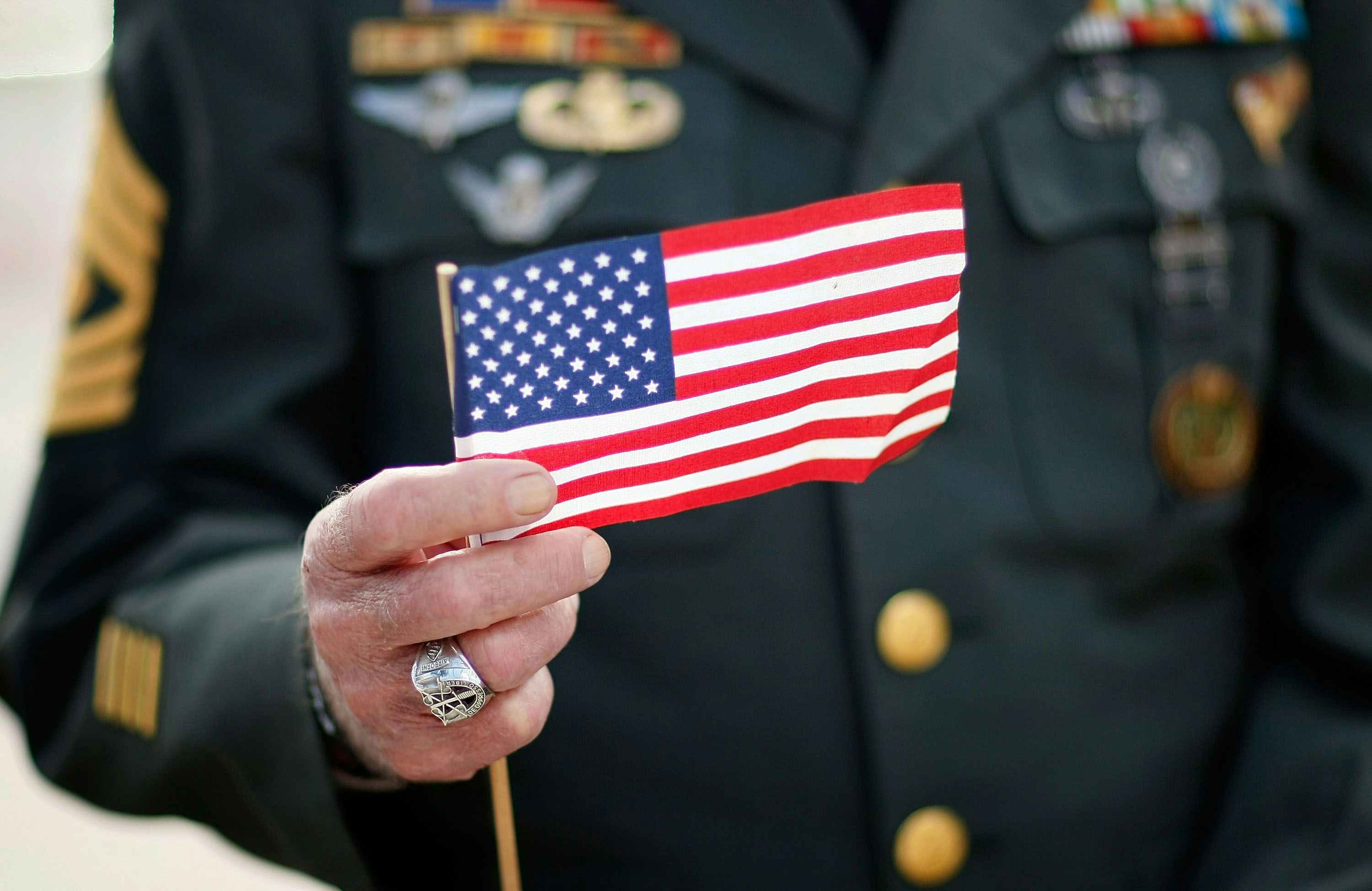A small American flag being held up by a military veteran in uniform.