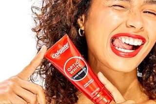 Person holding a tube of Colgate Optic White Toothpaste