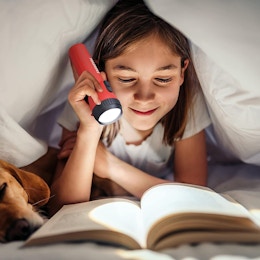 a kid reading a book with a red flashlight 