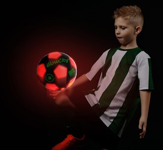a kid kicking a glowing red and black soccer ball