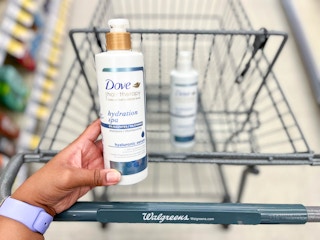 hand holding a bottle of Dove Hair Therapy Hydration Spa shampoo with conditioner in the cart behind it