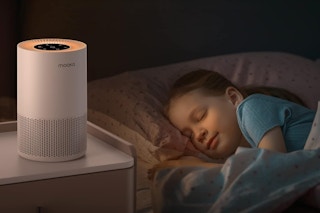 A Mooka Air Purifier with a night light sits on a night table next to a sleeping child.