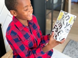 A child holding a Cards Against Humanity game and smiling.