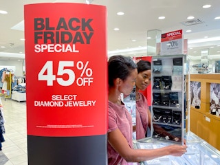 A 45% off Black Friday sign in a Macy's store next to a person looking at a display on the jewelry counter.