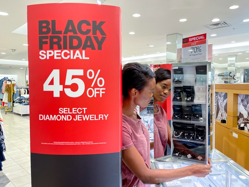 A 45% off Black Friday sign in a Macy's store next to a person looking at a display on the jewelry counter.