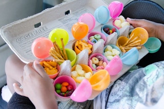 A child sitting in a car holding a cardboard egg carton filled with opened plastic Easter eggs on their lap. Each egg is filled with a ...