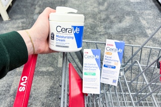 person holding cerave moisturizing cream over a cart with other cerave skincare products in it
