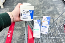 person holding cerave moisturizing cream over a cart with other cerave skincare products in it