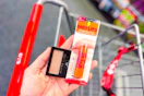 person holding maybelline eyeshadow and baby lips over a cart