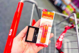 person holding maybelline eyeshadow and baby lips over a cart
