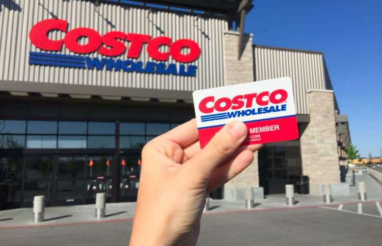Hand holding up Costco membership card in front of a Costco store