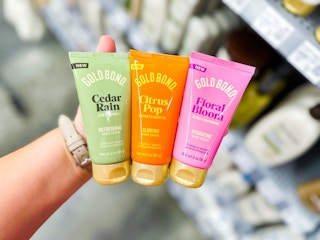 hand holding three bottles of gold bond scented hand cream in walmart aisle