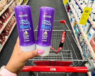 hand holding two bottles of Aussie 3 minute miracle moist deep conditioners in front of cart