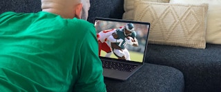 person lying on couch watching football on laptop