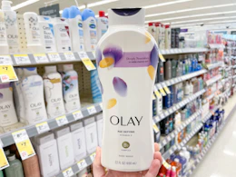 An Olay body wash held out by hand in front of store shelves with other body washes on them.