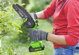 a person using a green mini chainsaw on a branch